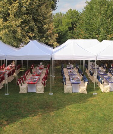 White 8x4 m Ecotent® folding gazebos as elegant cover for an outdoor banquet with decorated tables and chairs.