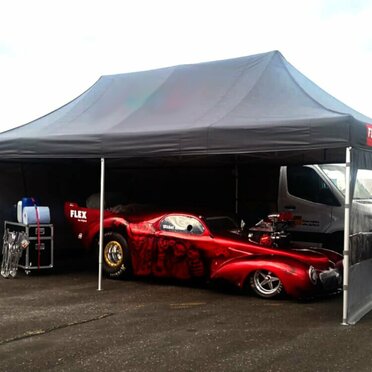 Black 6x4 m Ecotent® folding tent with FLEX branding used as a motorsport tent, featuring a red showcar and workshop equipment.