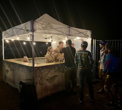 Ecotent® printed pop-up gazebo with leaf design, used as an outdoor bar at night with lights and people enjoying drinks.